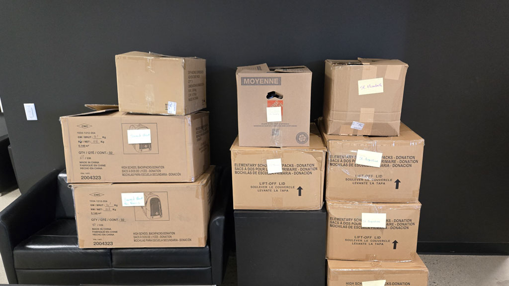 Many cardboard boxes filled with backpacks on display in the CEC lobby